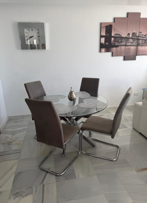 Modern dining area with round glass table, gray upholstered chairs, wall clock, and bridge photo in Costa Adeje apartment