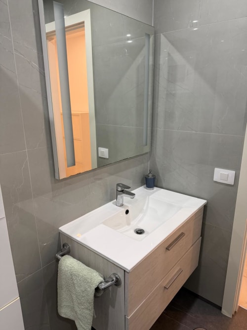 Modern bathroom with white sink vanity, gray tile walls, and mirror in Costa Adeje apartment near Siam Park