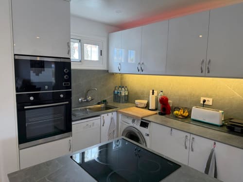 Modern kitchen in Costa Adeje apartment with white cabinets, black cooktop, yellow backsplash, and built-in appliances