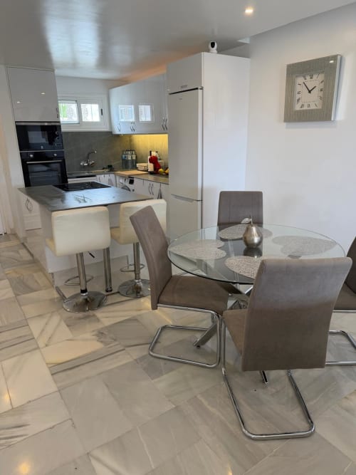 Modern kitchen-dining area in Costa Adeje apartment with white cabinetry, round glass table, brown chairs, and stainless