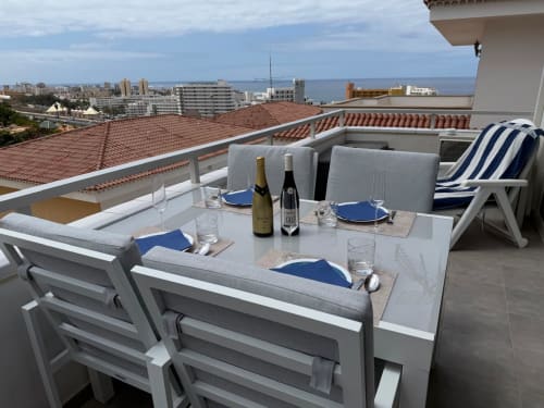 Rooftop terrace dining area in Costa Adeje with sea views, set table, wine bottles, and lounge chairs