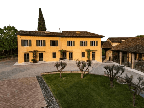 Hotel Relais Corte Baruzzo a Volta Mantovana con facciata gialla, cipressi, piante di olivo e corte interna.