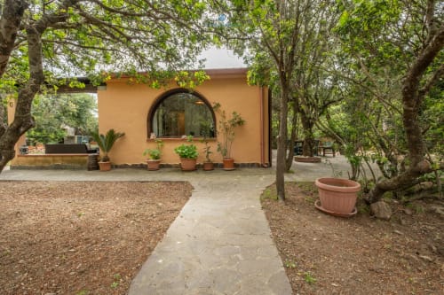 Ingresso del giardino di Villa Chia a Quartu Sant'Elena con costruzione in terracotta, vialetto in pietra e alberi secolari
