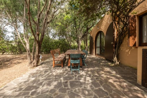 Patio ombreggiato con tavolo da pranzo e sedie sotto alberi centenari a Villa Chia, Quartu Sant'Elena
