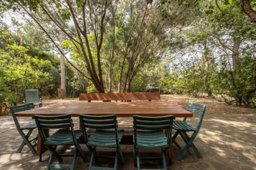 Area esterna per cenare a Villa Chia con tavolo in legno e sedie verdi sotto alberi alti a Quartu Sant'elena