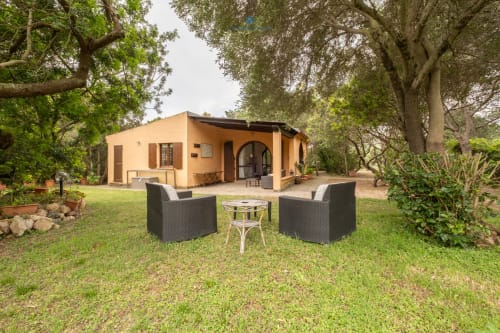 Vista del giardino di Villa Chia con zona sedute, casa arancione e alberi maturi a Quartu Sant'Elena