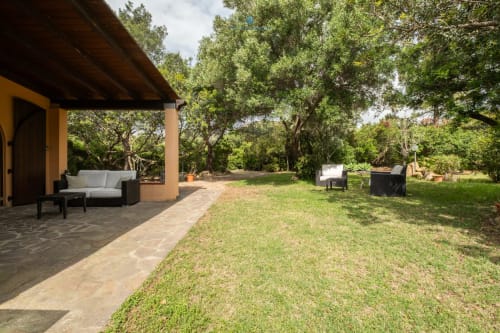 Giardino Villa Chia con patio arredato, prato verde rigoglioso, alberi maestosi e mobili da esterno a Quartu Sant'elena