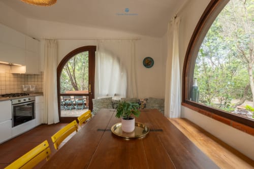 Ampia sala da pranzo di Villa Chia con tavolo in legno, sedie gialle, cucina e vista sul giardino attraverso grandi finestre