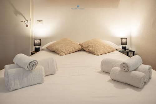 Spaziosa camera da letto della villa presso House Live Express con letto matrimoniale, cuscini beige, asciugamani arrotolati, lampade comodino e vista sul giardino