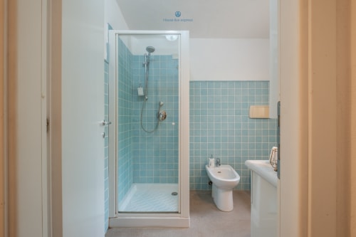Bagno moderno della villa House Live Express in Sardegna con doccia in piastrelle turchesi, bidet e lavabo con rubinetteria bianca