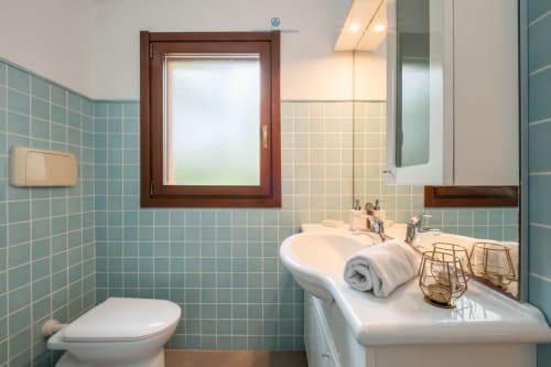 Bagno moderno di Villa Chia con piastrelle turchesi, lavabo bianco, WC e finestra satinata