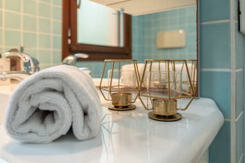 Bagno moderno della villa House Live Express con asciugamano arrotolato, lanterne decorative in ottone e pareti in piastrelle turchese