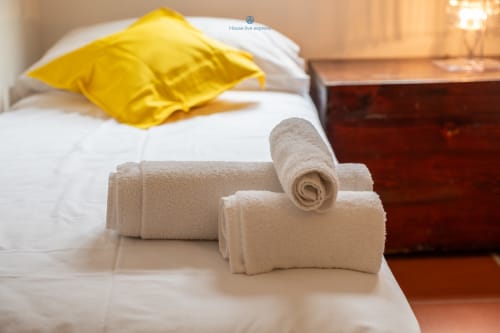 Asciugamani arrotolati e cuscino giallo su biancheria bianca nella camera da letto della villa House Live Express, Quartu Sant'elena
