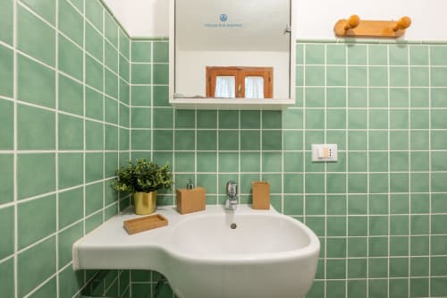 Bagno moderno con piastrelle verdi, lavabo bianco su piedistallo, accessori in legno e specchio della villa House Live Express
