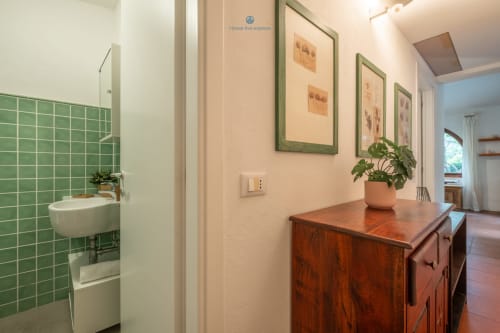 Corridoio della villa House Live Express con cassapanca in legno, pianta in vaso e bagno con piastrelle verdi, Quartu Sant'elena