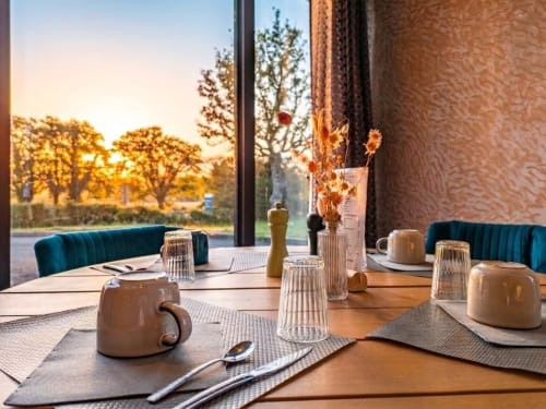 Table de salle à manger élégante à l'hôtel La Verriaire avec vue sur le coucher de soleil et les jardins de la campagne française