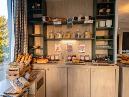 Vitrine de boulangerie de l'hôtel La Verriaire avec pain frais, pâtisseries, pots de miel et tartinades sur des étagères en bois