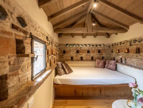 Junior Suite presso Corte Baruzzo Relais con muri in pietra, soffitto con travi in legno e letto con vista sul giardino a Volta Mantovana