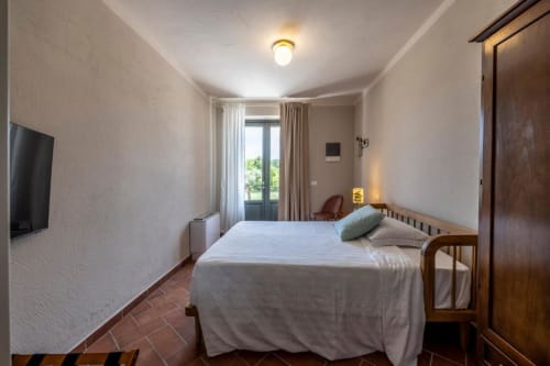 Camera luminosa al Corte Baruzzo Relais con biancheria bianca, letto in legno, TV a schermo piatto e vista sul giardino