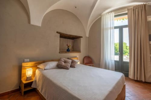 Camera confortevole al Corte Baruzzo Relais di Volta Mantovana con soffitti a volta, letto, comodino in legno e vista sulla corte