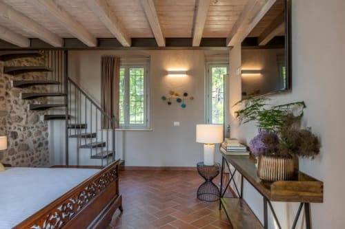 Suite elegante a Corte Baruzzo Relais con travi a vista, scala a spirale, finestre con vista sul giardino e arredi moderni.
