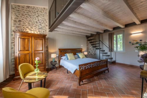 Suite spaziosa presso Corte Baruzzo Relais con letto in legno, muri in pietra, scala a chiocciola, pavimenti in cotto e vista sul giardino