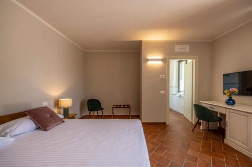 Camera accogliente al Corte Baruzzo Relais con letto, scrivania, TV e pavimento in cotto che si affaccia sulla corte interna