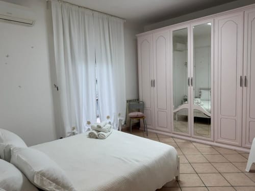 Camera da letto spaziosa dell'Appartamento Catan Nìá con armadio rosa, letto bianco e luce naturale dalla finestra con tende