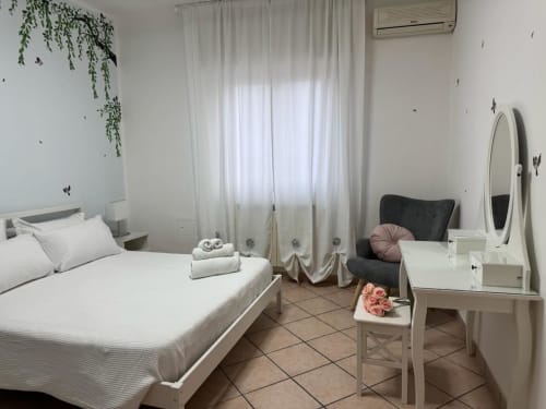 Camera moderna all'Appartamento Catan Nià di Catania con letto bianco, toletta, poltrona e piante sospese