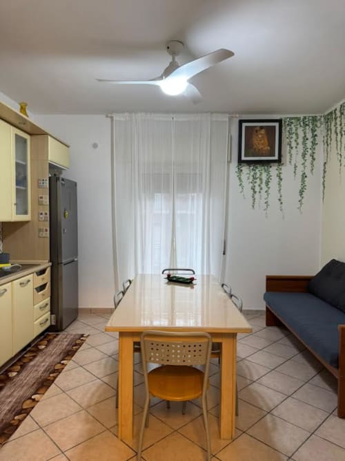 Ampia zona cucina-soggiorno nell'Appartamento Catan Nìa, Catania con mobili gialli, tavolo da pranzo e ventilatore moderno.
