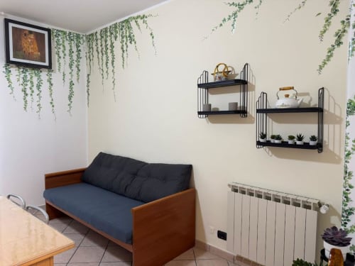 Accogliente salotto di appartamento a Catania con divano in legno, mensole a muro, piante sospese e radiatore