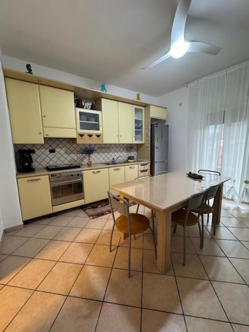 Cucina gialla e luminosa con tavolo da pranzo nell'appartamento di Catania. Elettrodomestici moderni, pavimento in piastrelle, ventilatore a soffitto.
