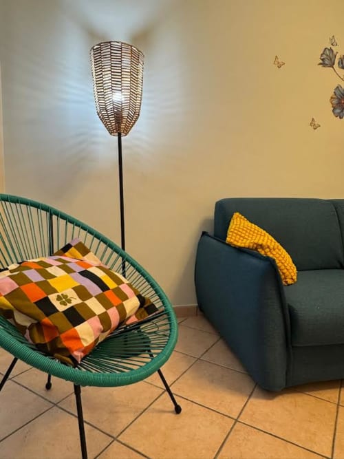 Interno colorato dell'appartamento con sedia intrecciata verde, cuscino patterned, divano scuro e lampada a stelo presso Catan Appartament Nìa©