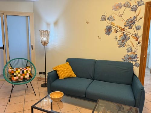 Moderna camera da letto dell'Appartamento Nià a Catania con divano scuro, poltrona turchese e decorazioni floreali