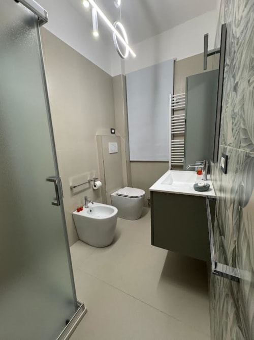 Bagno moderno all'Appartamento Nìa di Catania con lavabo bianco, water, bidet, scaldasalviette e finiture in legno