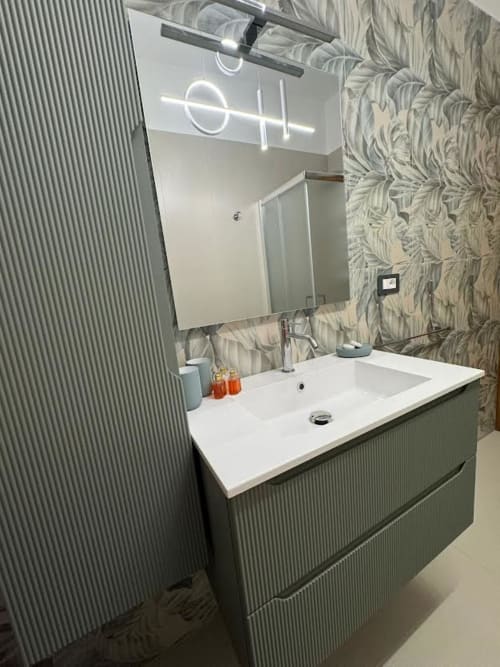 Bagno moderno nell'Appartamento Niá a Catania con lavabo bianco, vanity verde, insegna al neon e carta da parati decorativa