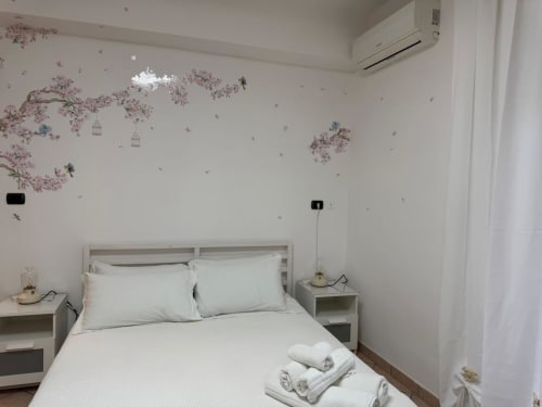 Camera moderna al Catan Appartament di Catania con letto bianco, comodini e murale con fiori di ciliegio