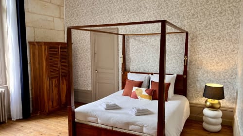 Chambre élégante au Domaine du Faure avec lit à baldaquin en acajou, draps blancs, papier peint à motifs et armoire en bois
