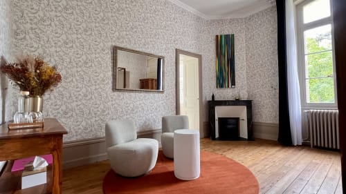 Élégant salon du Domaine du Faure avec fauteuils crème, cheminée, papier peint à motifs et vue sur le jardin