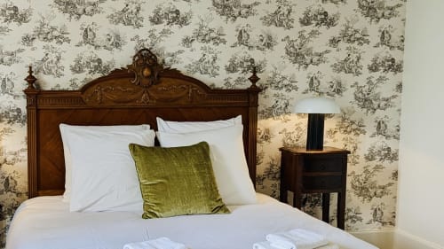 Suite élégante du Domaine du Faure avec lit en bois ouvragé, linge blanc et papier peint à motif de jardin
