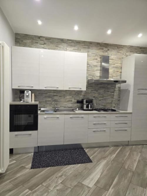 Cucina moderna nell'appartamento Mia Experience a Monza con mobili bianchi, rivestimento in piastrelle grigie e elettrodomestici in acciaio inossidabile