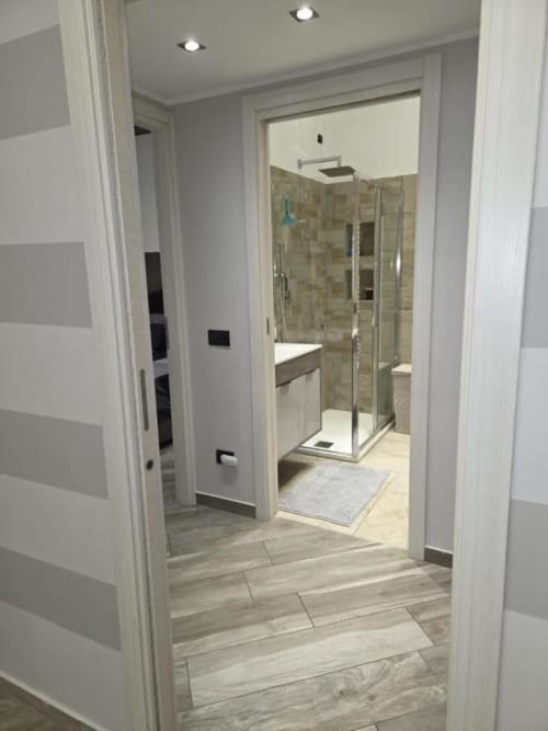 Bagno moderno dell'appartamento Mia Experience a Monza con doccia in vetro, piastrelle e pavimento effetto legno