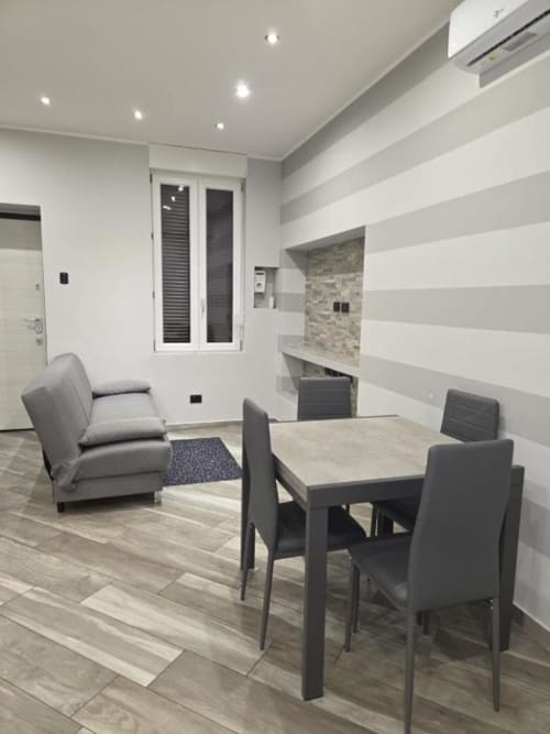 Soggiorno moderno presso Mia Experience Monza con tavolo da pranzo, sedie grigie, poltrona lounge e parete a righe