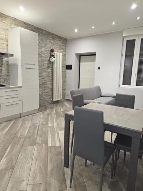 Zona living moderna con tavolo da pranzo, sedie grigie, cucina con ante bianche e pavimenti in legno nell'appartamento Mia Experience,