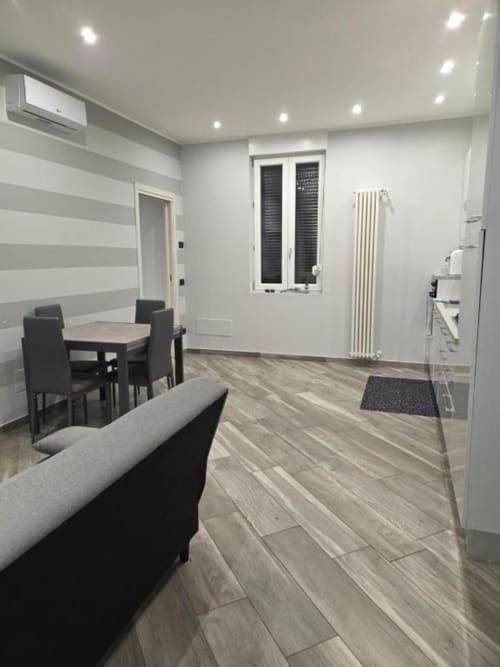 Soggiorno moderno nell'appartamento Mia Experience a Monza, con tavolo da pranzo, divano grigio, pavimento in legno e arredamento contemporaneo a righe