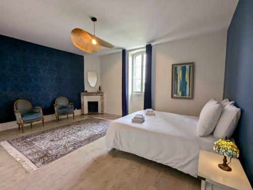 Suite élégante Le Faure au Domaine du Faure avec lit king-size, cheminée, mur d'accent bleu et coin salon avec vue sur le jardin
