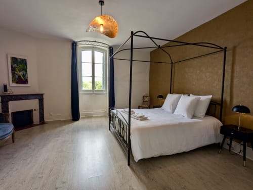 Suite élégante au Domaine du Faure avec lit à baldaquin, luminaire or contemporain, cheminée et vue sur le jardin