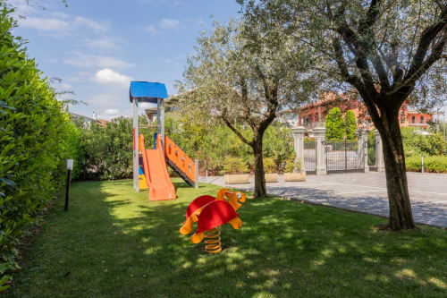Area giochi per bambini dell'hotel Prince Garda a Serniga con scivolo, altalena a molla e ulivi