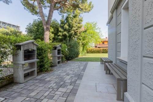Terrazza esterna dell'hotel Prince Garda a Serniga con sedute in cemento, griglie integrate e vista sul rigoglioso giardino