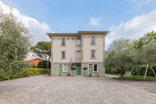 Hotel Prince Garda a Serniga: facciata beige, porte verdi, corte pavimentata e giardini circostanti